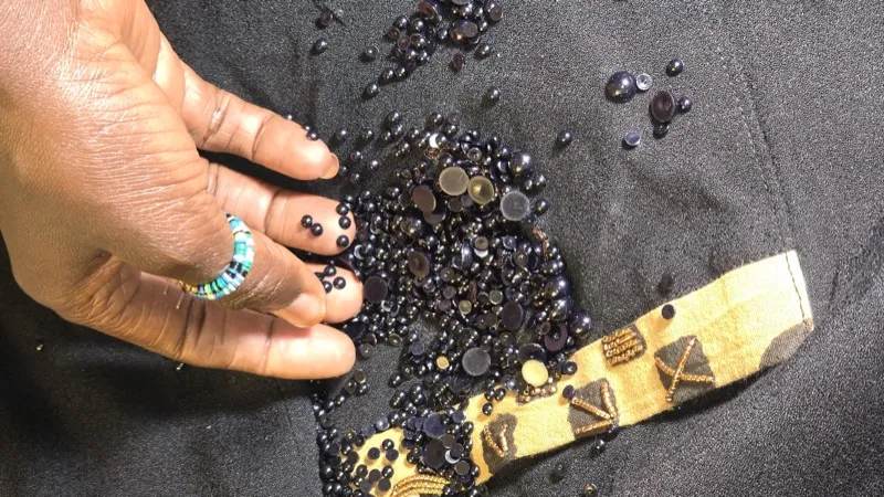 Hand sorting black beads on dark fabric with bogolan strip